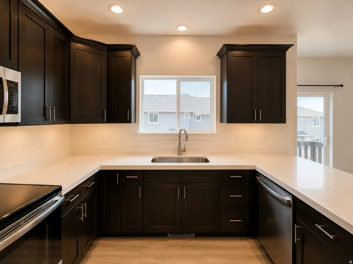 Modern kitchen featuring dark wood cabinetry, light-toned countertops, and a stainless steel undermount sink