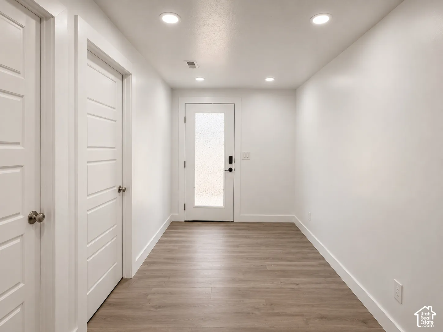 Hallway featuring wood-finish flooring, recessed lighting, and a white interior door with frosted glass paneling
