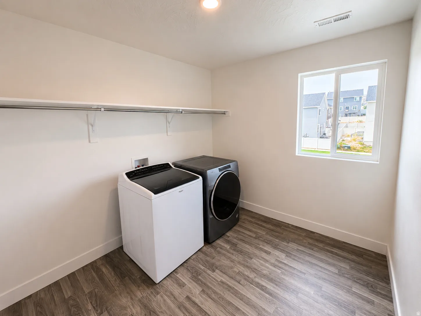 Utility room with wood-finish flooring, a white trim baseboard, and a white framed window