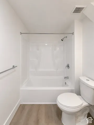 Bright bathroom featuring a white tub and shower combination with chrome fixtures, a white toilet, and wood-finish flooring