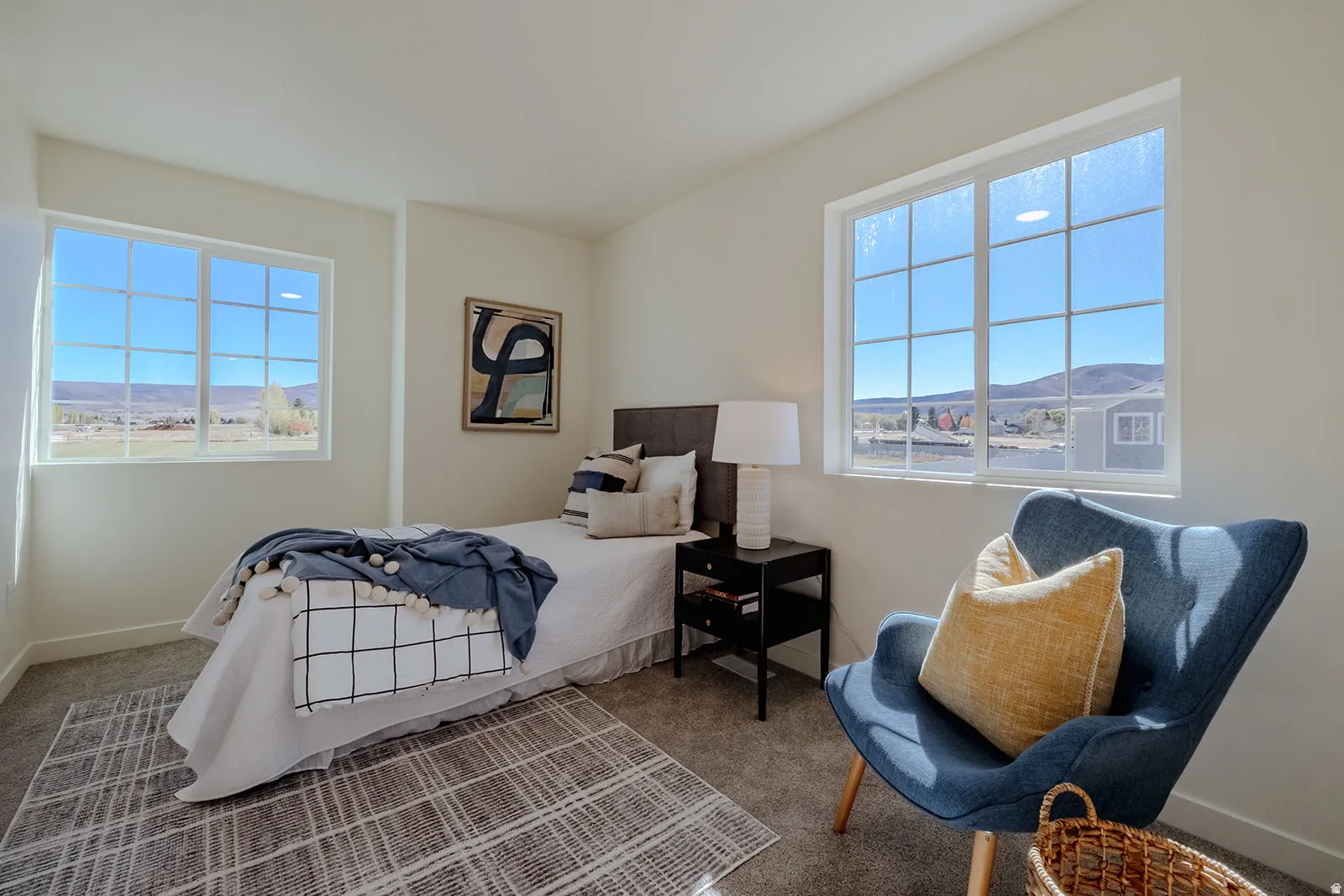 Light-filled room featuring two large grid-pattern windows, neutral wall tones, and soft grey carpet flooring