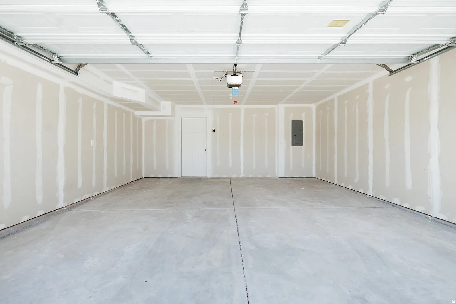 Spacious garage featuring a concrete floor, unpainted drywall walls, a single white entry door, and an overhead garage door mechanism