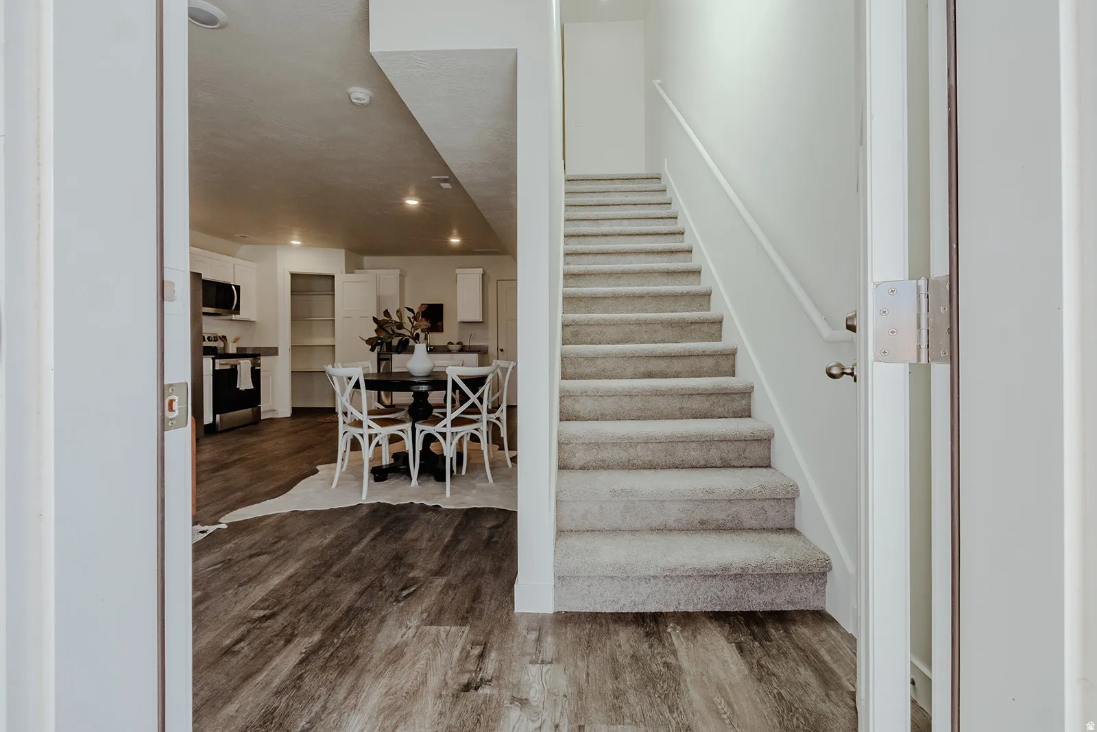 Carpeted staircase with white handrail and wood-finish flooring extending into the dining area and kitchen featuring white cabinetry and built-in shelving