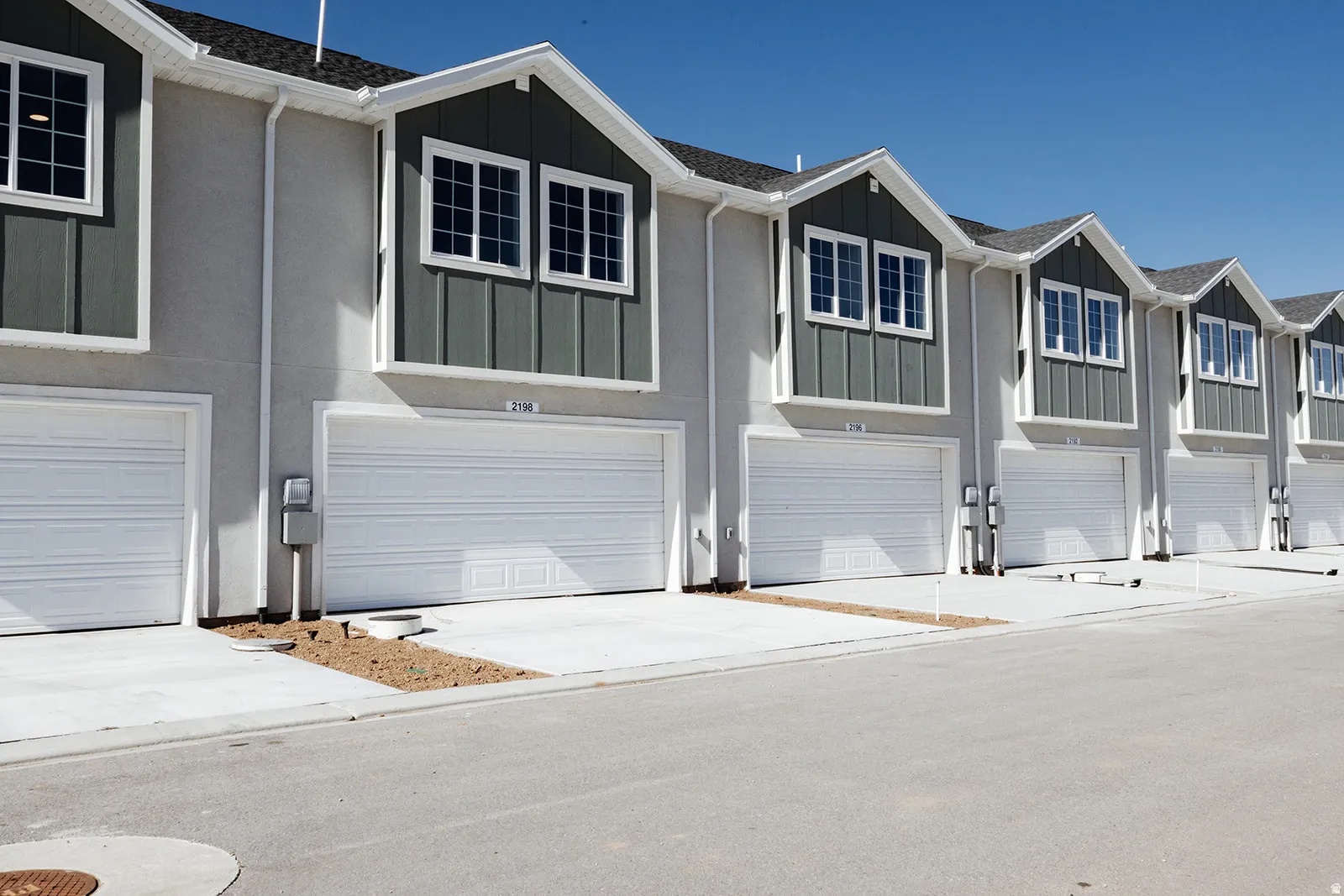 Row of townhomes featuring stucco and vertical siding exteriors, individual attached garages, white window frames, and concrete driveways