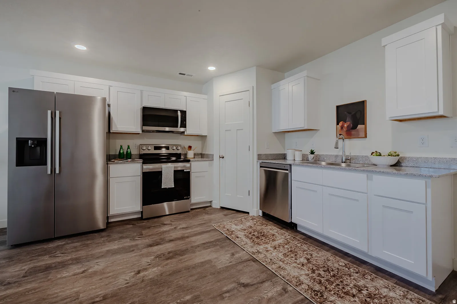 Modern kitchen with wood-finish flooring, white cabinetry, and stainless steel appliances