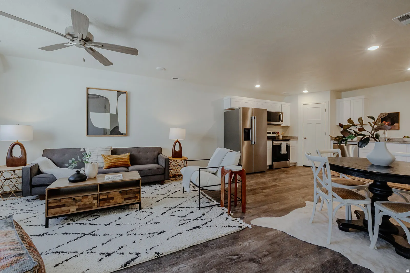 Open-concept living space featuring wood-finish flooring, a contemporary ceiling fan, and white walls