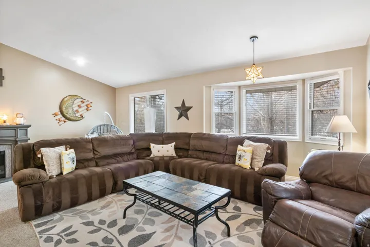 Living room featuring a glass covered fireplace, light colored carpet, vaulted ceiling, and plenty of natural light