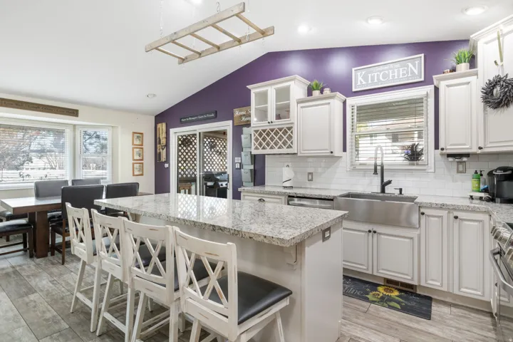 Kitchen with vaulted ceiling, a kitchen breakfast bar, glass insert cabinets, a center island, and light stone countertops