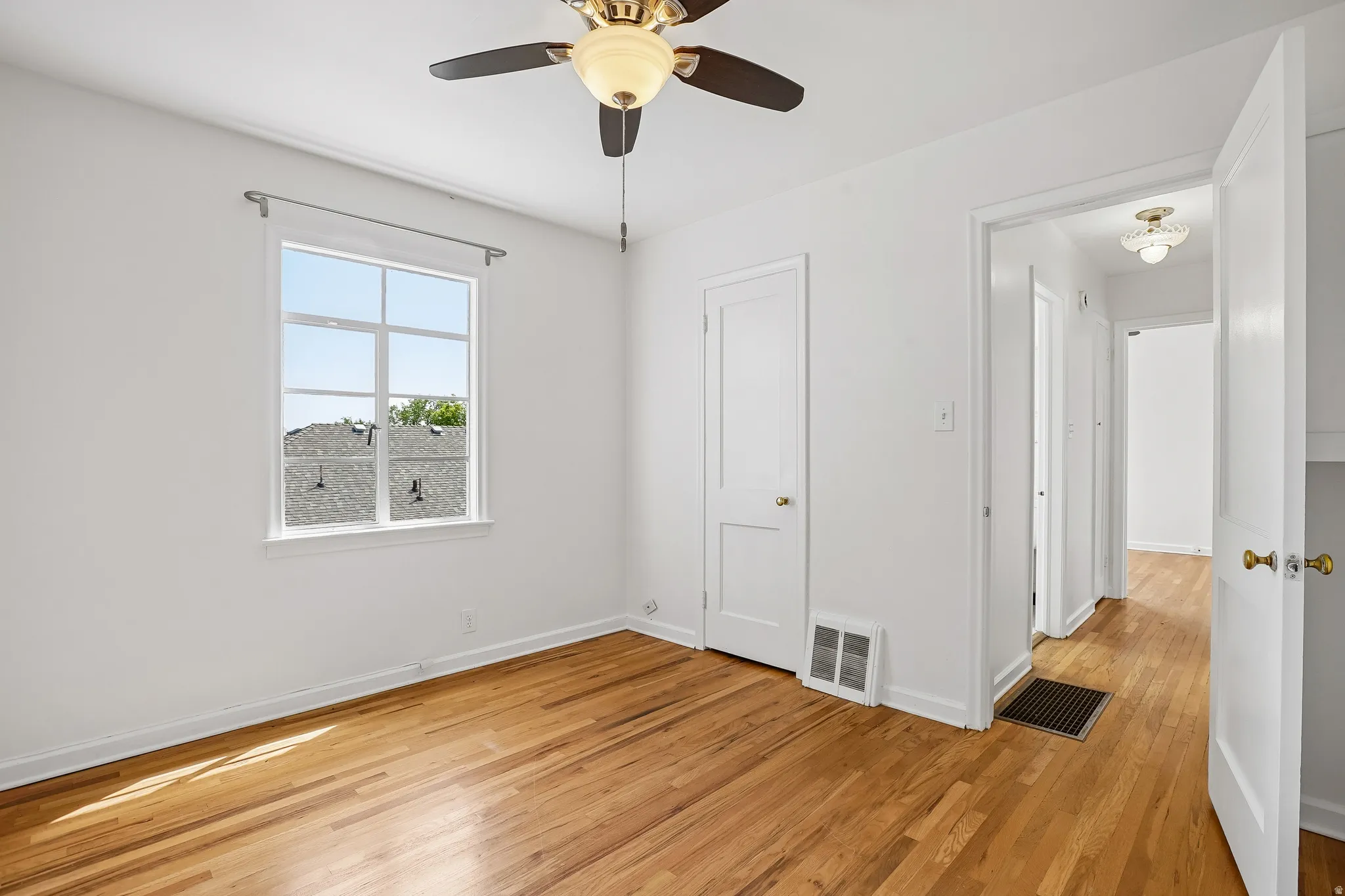 Bright room featuring wood flooring, a ceiling fan, a window, and white interior doors
