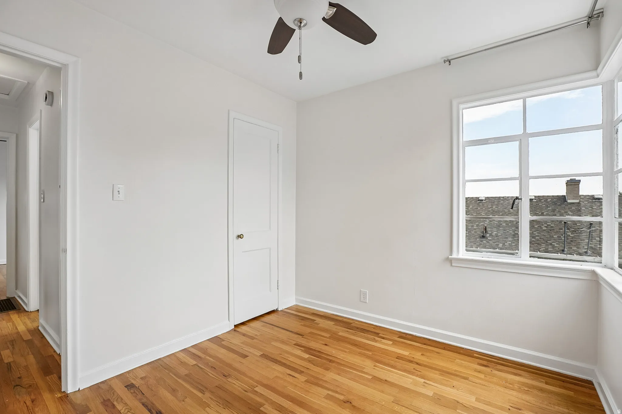 Bright room featuring hardwood flooring, white walls, a multi-pane window, and a ceiling fan