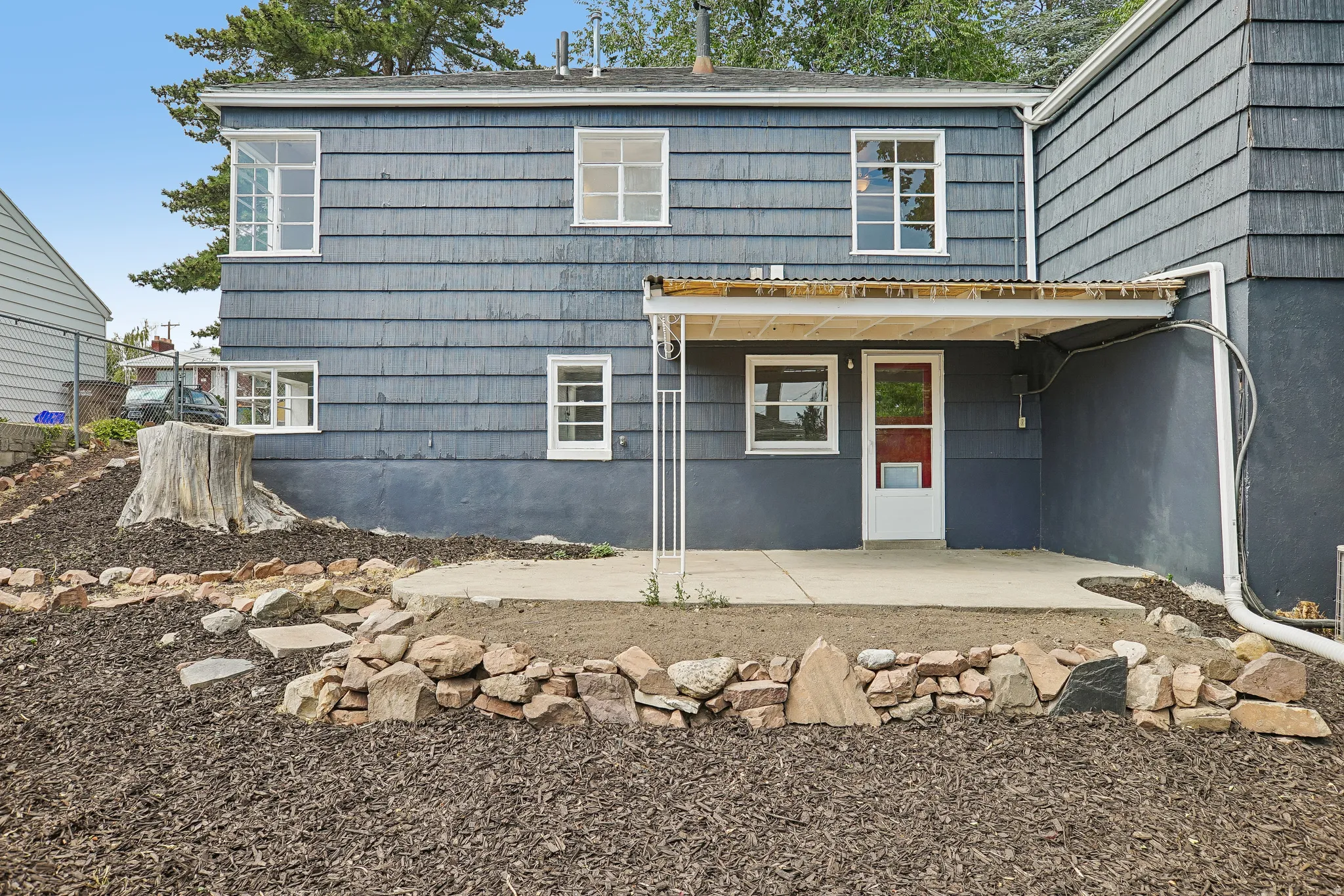Rear exterior featuring shingle siding, multiple windows, a concrete patio, and a covered entry with a red door