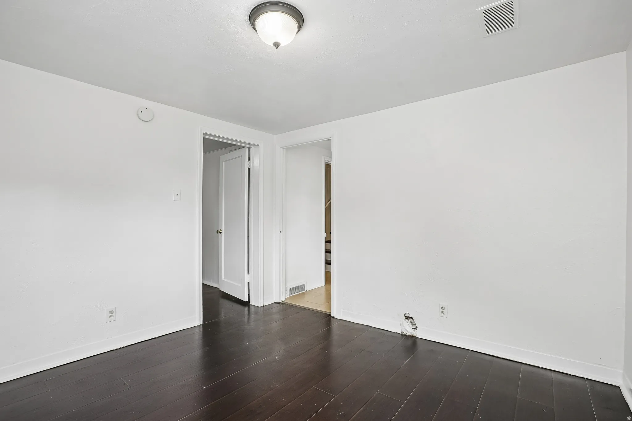 Interior room featuring dark wood-finish flooring, white walls, and a ceiling-mounted light fixture