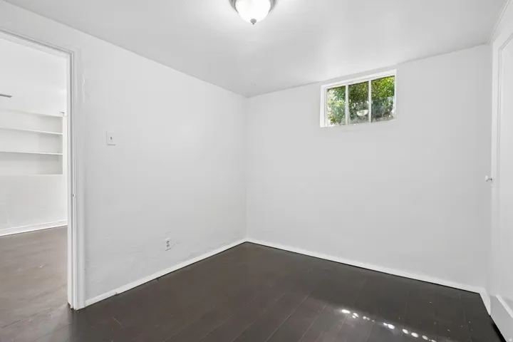 Room with dark wood-finish flooring, white painted walls, and a single window