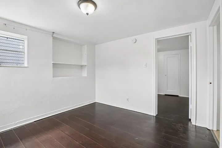 Room featuring dark wood-finish flooring, built-in shelving, white painted walls, and a window with blinds