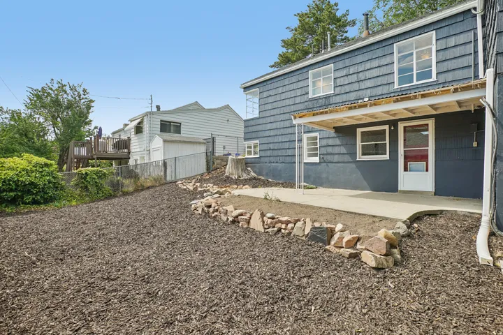 Expansive mulched outdoor space featuring a concrete patio, covered porch, and rock-lined landscaping