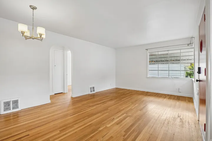 Expansive room featuring wood-finish flooring, a contemporary four-light chandelier, a multi-pane window, and an arched entryway