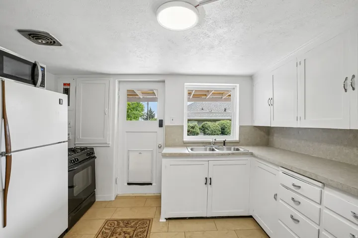 Kitchen featuring white cabinetry, a double basin stainless steel sink, light-toned countertops with a matching backsplash, and tile flooring
