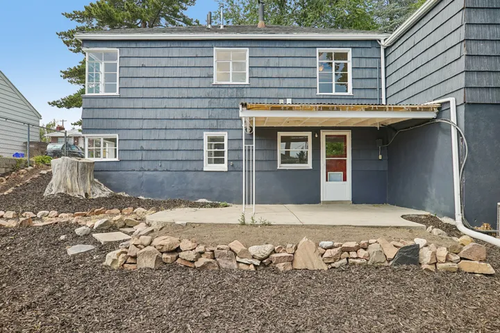 Rear exterior featuring shingle siding, multiple windows, a concrete patio, and a covered entry with a red door