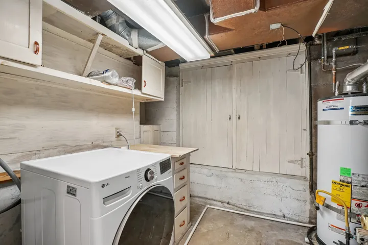 Utility space featuring overhead shelving, built-in cabinetry, concrete flooring, and a visible water heater