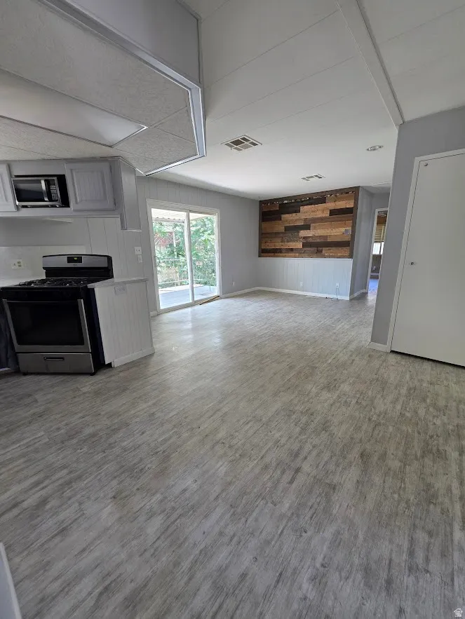Spacious open-concept living area featuring wood-finish flooring, a contemporary wood-panel accent wall, and sliding glass doors