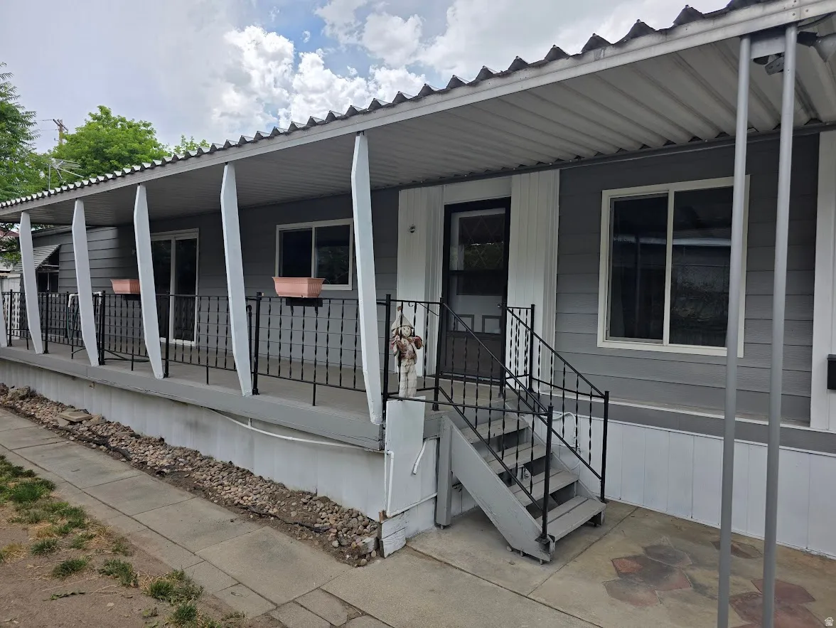 Front exterior featuring a covered porch with a corrugated metal roof, gray siding, white trim, and black wrought iron railings