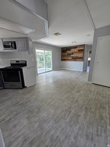 Spacious open-concept living area featuring wood-finish flooring, a contemporary wood-panel accent wall, and sliding glass doors