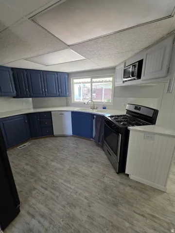 Kitchen featuring blue and white cabinetry, white countertops, stainless steel appliances, wood-finish flooring, and a large window