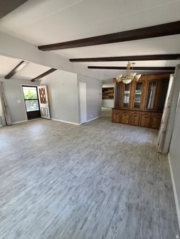 Spacious interior featuring light wood-finish flooring, exposed ceiling beams, and a built-in wood-finish hutch with glass-front cabinetry