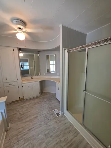 Bathroom featuring a glass-enclosed shower, wood-finish flooring, a vanity with integrated sink, built-in cabinetry, and a ceiling fan