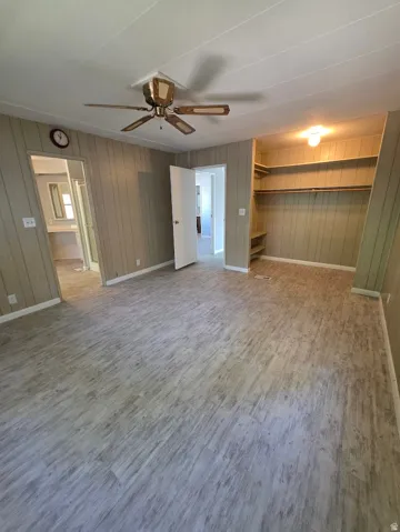 Spacious room featuring wood-finish flooring, vertical paneling, and an open closet with built-in shelving