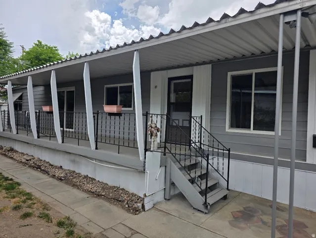 Front exterior featuring a covered porch with a corrugated metal roof, gray siding, white trim, and black wrought iron railings