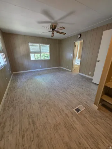 Spacious interior featuring wood-finish flooring, two windows with blinds, and a ceiling fan with integrated lighting