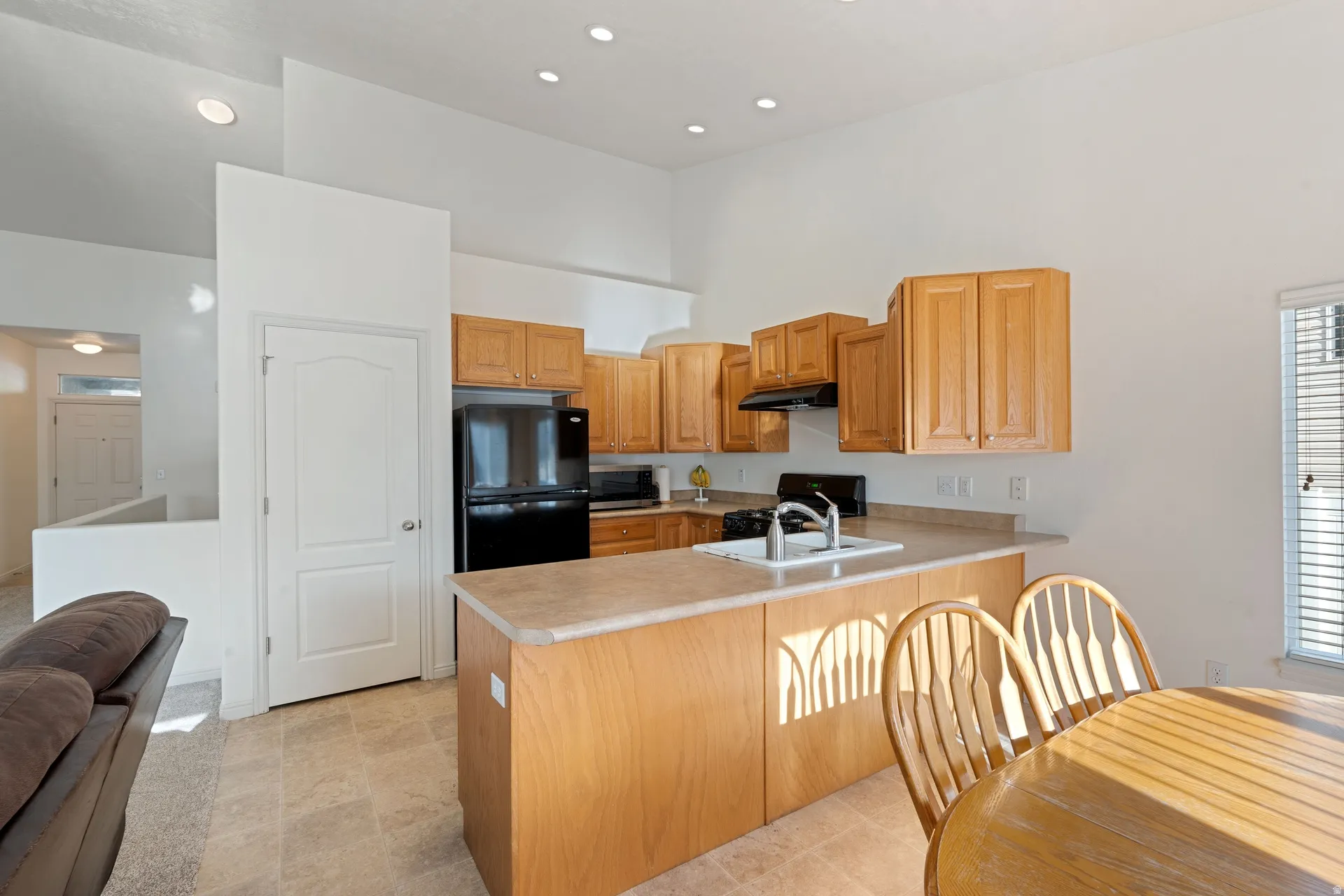 Kitchen featuring light wood cabinetry, black appliances, a double basin sink, and an island with countertop seating