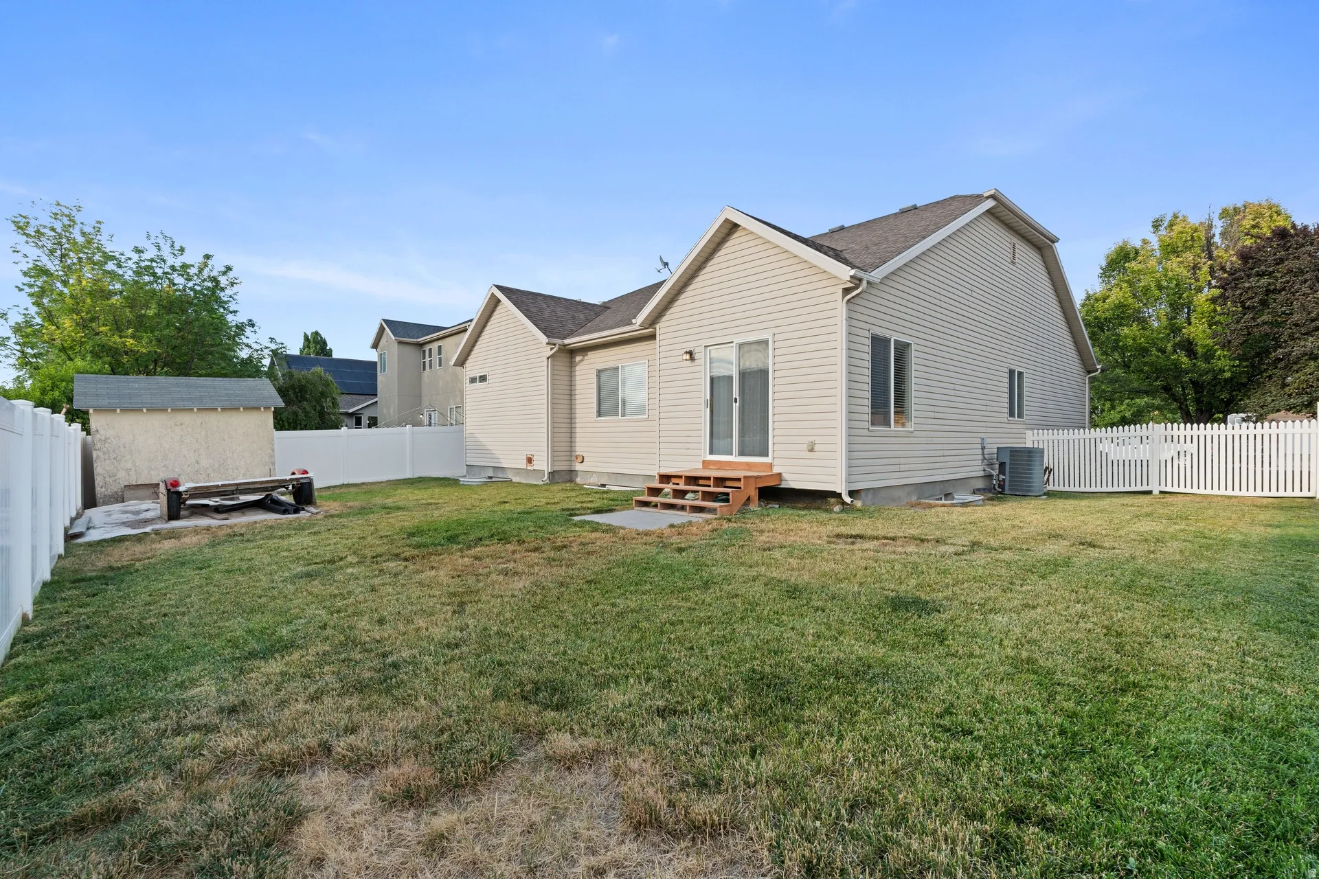Expansive backyard featuring a manicured lawn, a white vinyl privacy fence, and a white picket fence segment