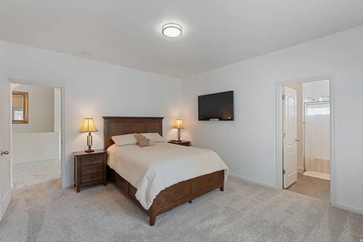 Carpeted bedroom featuring a flush-mount ceiling light and a white paneled door leading to a bathroom with a shower