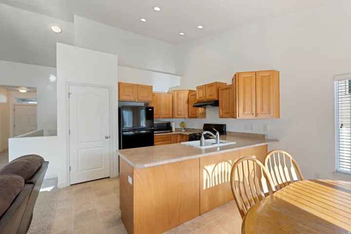 Kitchen featuring light wood cabinetry, black appliances, a double basin sink, and an island with countertop seating