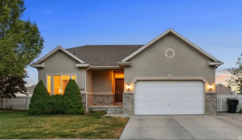 Stucco exterior with stone accents, featuring a two-car garage, a covered entryway, and a white picket fence