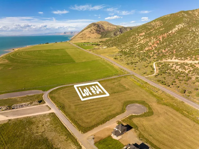 Expansive undeveloped lot featuring surrounding green fields, a paved road, and distant mountain terrain