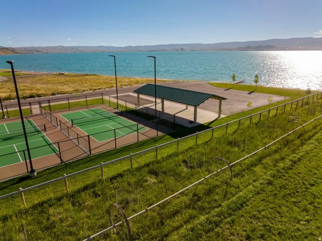 Recreational courts with a green surface and perimeter fencing, complemented by a covered open-air structure