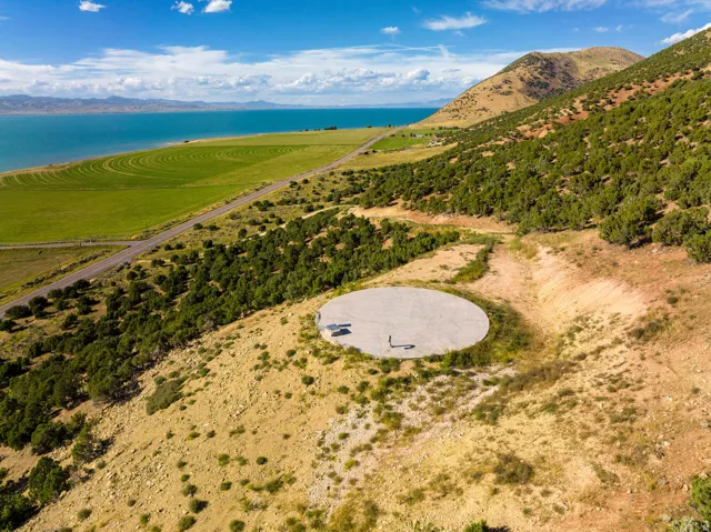 Expansive land parcel featuring a large circular concrete pad, surrounded by natural scrub brush and evergreen trees