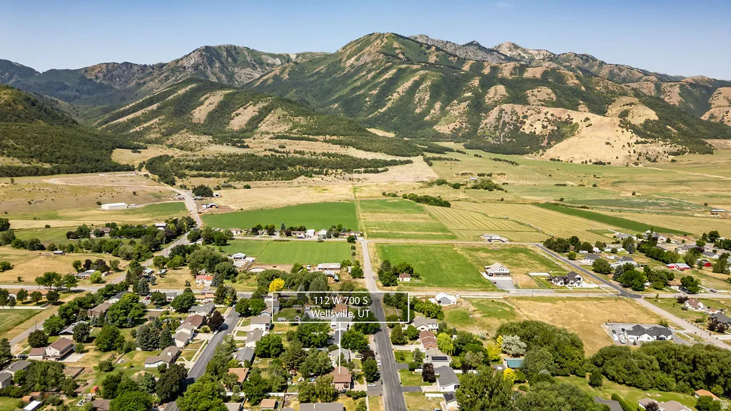 Aerial perspective showcasing a residential area with established trees and surrounding agricultural land, set against a backdrop of prominent mountains