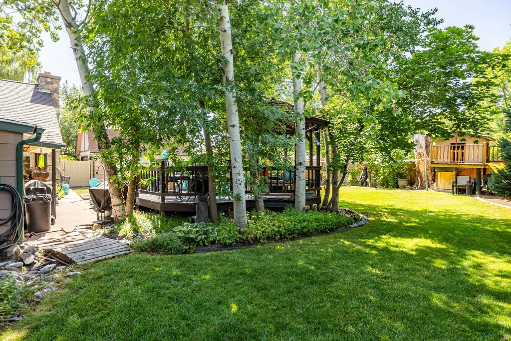 Expansive green lawn with mature trees, featuring a raised wooden deck with a gazebo, and a secondary multi-level wooden structure