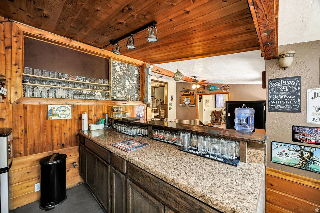 Rustic wood-paneled bar featuring a speckled countertop, built-in shelving, and track lighting