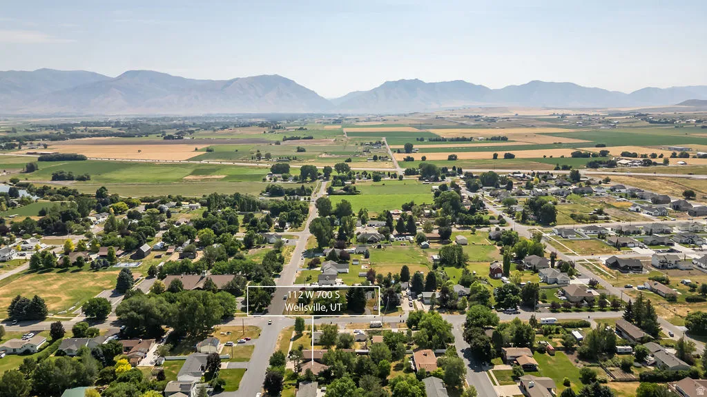 Expansive aerial perspective showcasing a residential neighborhood with surrounding agricultural fields and distant mountain ranges