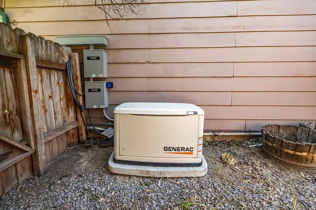 Exterior showcasing a Generac whole-house generator on a concrete pad, electrical conduit, and utility boxes, positioned alongside timber fencing and gravel ground cover