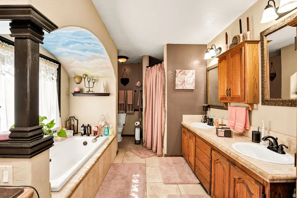 Bathroom featuring a built-in tub with an arched alcove, dual vanity with wood cabinetry, and a separate commode area