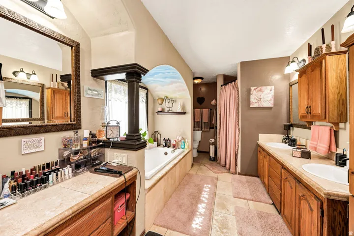 Bathroom featuring dual vanities with integrated sinks, a built-in bathtub with a decorative archway, wood-finish cabinetry, and tiled flooring