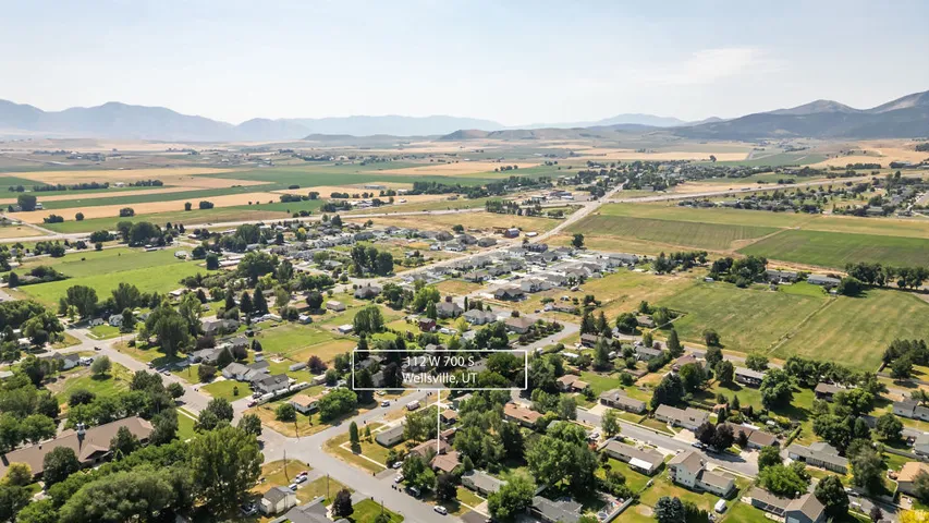Aerial perspective showcasing the property within a residential neighborhood featuring mature trees, surrounded by expansive agricultural fields