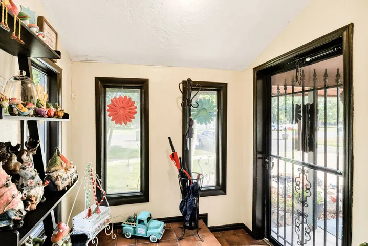 Entryway featuring a security screen door, two vertical windows with dark trim, light-colored walls, and terracotta-style floor tiles