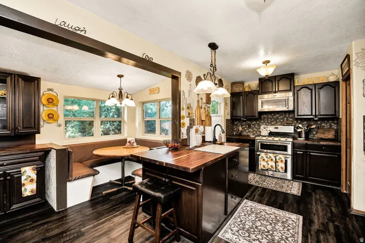 Kitchen featuring dark wood-finish cabinetry, stainless steel appliances, dark wood-finish flooring, a built-in banquette seating area, and a central island with a wood countertop